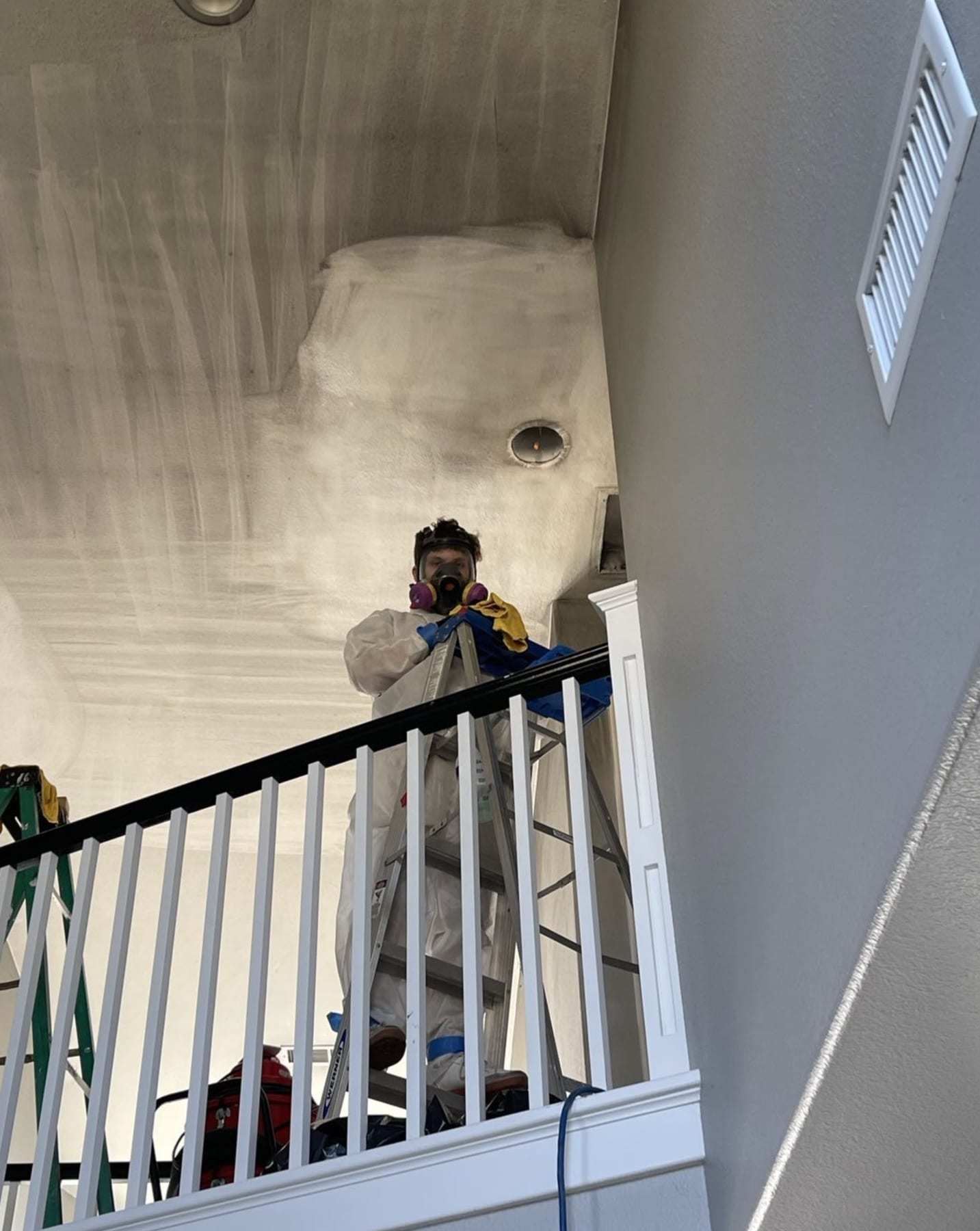 Technician on a ladder treating a ceiling above a stair railing