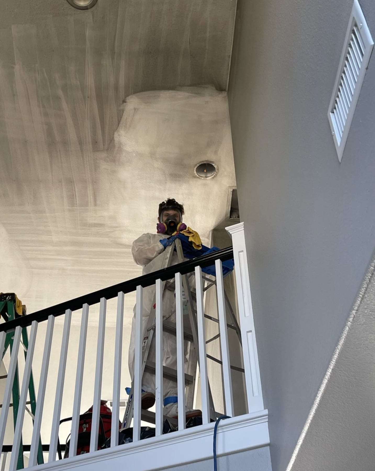 Technician on a ladder treating a ceiling above a stair railing